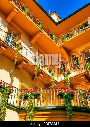 Wunderschöne Fassade des europäischen Gebäudes mit bunten Blumenkästen auf Balkonen unter dem blauen Himmel, lebhafte Architektur mit hängenden Pflanzen und Sommersonnenlicht, Außenansicht des Hauses im italienischen oder mediterranen Stil Stockfoto