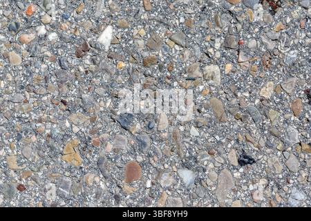 Nahaufnahme einer grauen Oberfläche eingebettet mit verschiedenen kleinen Felsen und Kieselsteinen in verschiedenen Formen, Größen und Farben. Stockfoto