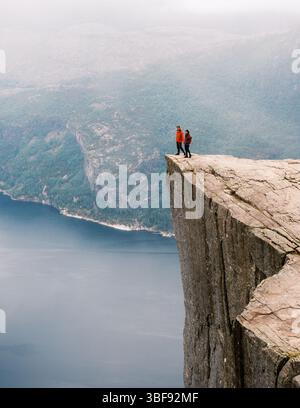 Zwei Wanderer stehen auf dem berühmten Preikestolen Pulpit Rock und blicken über den atemberaubenden Fjord darunter. Umgeben von dramatischen Klippen und üppigem Grün in Norwegen Stockfoto
