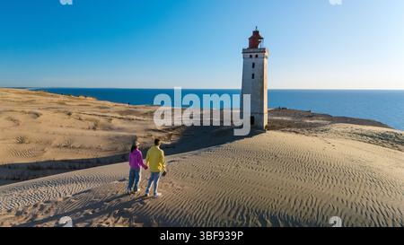 Ein Paar steht Hand in Hand und blickt auf den markanten Leuchtturm inmitten von sanften Sanddünen entlang der atemberaubenden dänischen Küste. Rubjerg Knude Leuchtturm Nordjütland Dänemark Stockfoto
