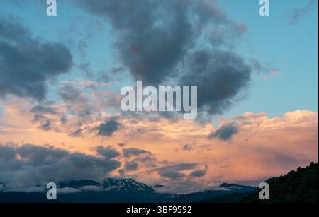 Atemberaubender Blick auf einen dramatischen Wolkenhimmel, beleuchtet von warmen Sonnenuntergangsfarben über schneebedeckten Bergen, ruhige Kulisse, für Hintergründe und Wallpa Stockfoto