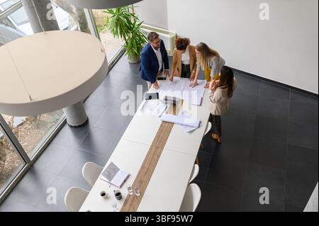 Hochwinkelansicht professioneller Ingenieure, die Baupläne analysieren und an neuen Projekten im Besprechungsraum arbeiten Stockfoto