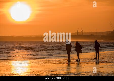 Die untergehende Sonne vom Brighton Beach aus gesehen. Menschen, die die Ebbe bei Sonnenuntergang genießen. Fotografiert vom Brighton Beach mit Blick nach Westen über Hove. Brighton und Hove, England, Großbritannien Stockfoto