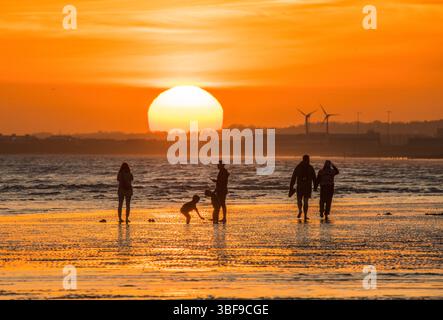 Die untergehende Sonne vom Brighton Beach aus gesehen. Die Familie genießt die Ebbe bei Sonnenuntergang. Fotografiert vom Brighton Beach mit Blick nach Westen über Hove. Brighton und Hove, England, Großbritannien Stockfoto