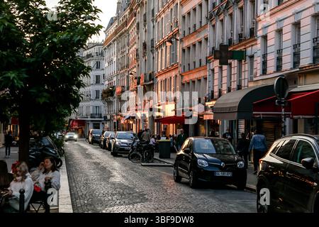Die belebte Rue des Abbesses in Paris wird am Abend zum Leben erweckt, mit Spaziergängen, Restaurants in Cafés im Freien und Geschäften wie „Fromagerie“. Stockfoto