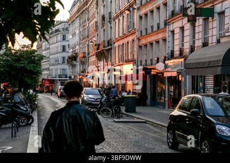 Die belebte Rue des Abbesses in Paris wird am Abend zum Leben erweckt, mit Spaziergängen, Restaurants in Cafés im Freien und Geschäften wie „Fromagerie“. Stockfoto