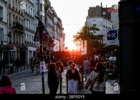 Belebte Pariser Straßenszene bei einem pulsierenden Sonnenuntergang, voller Menschen, die in Cafés im Freien spazieren und sitzen, in das warme, goldene Licht getaucht sind Stockfoto