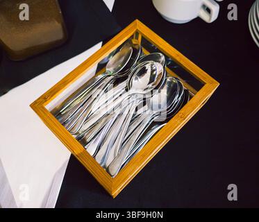 Teelöffel aus Metall in einer Holzkiste – Einrichtung von Catering-Utensilien Stockfoto