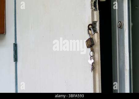 Eine Nahaufnahme einer offenen Tür mit einem Vorhängeschloss und Schlüsseln, die am Griff hängen. Dieses Bild symbolisiert Sicherheit, Zugang und Neuanfänge in einer Residentia Stockfoto