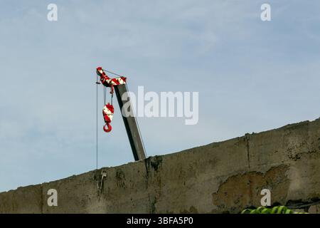 Eine Baustellenszene mit einem Kran mit rotem Haken vor blauem Himmel, der die städtische Entwicklung und die industrielle Tätigkeit von bui hervorhebt Stockfoto