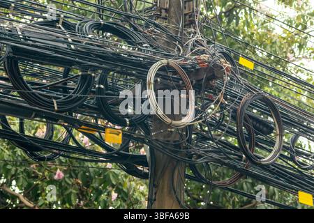 Eine chaotische Anordnung von elektrischen Leitungen an einem Versorgungsmast, die die Komplexität der städtischen Infrastruktur und der technologischen Verbindungen in der Stadt verdeutlicht Stockfoto