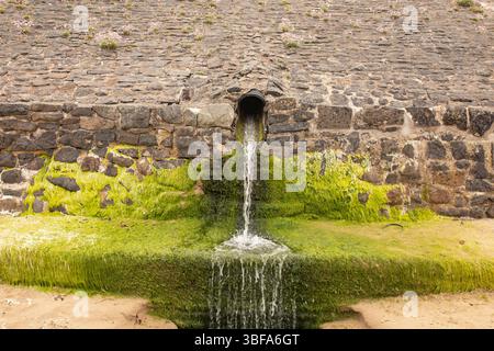 Abflussrohr für Sturmabwasser, das Wasser auf einen Sandstrand ableitet. Konzept der Qualität der Küstengewässer. Stockfoto