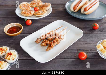 Gegrillte Yakitori-Hähnchenspieße auf einem weißen Teller, umgeben von Eiern, Käsewürfeln und Snacks. Bier-Snack, Partyessen Stockfoto