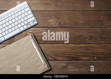 Stillleben des Büroarbeitsplatzes mit Zubehör. Flacher alter Holztisch mit weißer Computertastatur, Stift und Notebook. Geschäftskonzept von oben. Vint Stockfoto