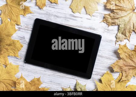 Tablet-Computer mit leerem Bildschirm liegt auf Vintage-Holztisch mit hellem Laub. Flache Lay-Komposition mit Herbstblättern auf weißer Holzoberfläche. Zoll Stockfoto