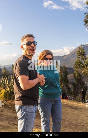 Ein Mann und eine Frau stehen auf einem Hügel, lächeln und halten Hände. Die Szene ist friedlich und ruhig, mit einem wunderschönen Blick auf die Berge in der Stockfoto