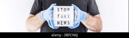 Fake News Infosemics during Covid-19 Pandemie Concept. Mann trägt Schutzmaske und medizinische Handschuhe an den Händen halten Leuchtkasten mit Text Stop Fake ne ne Stockfoto