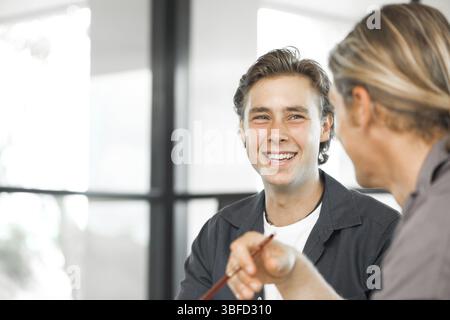 Junge Kollegen sitzen am Schreibtisch und diskutieren im hellen Büro Stockfoto