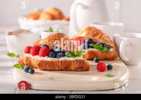 Heißes und hausgemachtes französisches Croissant mit Himbeeren und Heidelbeeren. Croissants als frisches Sandwich mit Beeren. Stockfoto