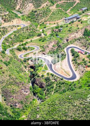 Aus der Vogelperspektive auf die Serpentinenstraße in der Bergschlucht des Vorotan River mit Teufelsbrücke, zwischen den Dörfern Tatev und Halidzor von der Seilbahn Wings of Tatev Stockfoto
