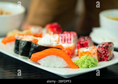 Bunte Auswahl an authentischen Sushi-Brötchen und Nigiri mit frischen Meeresfrüchten. Schöne Präsentation von nahrhaftem japanischem Fast Food. Stockfoto