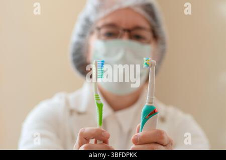 Nahaufnahme einer Zahnarztin, die eine Handzahnbürste in der einen Hand und eine elektrische in der anderen Hand hält. Ein visueller Leitfaden zur Mundhygiene, Zahntechnik und Zahnpflege. Stockfoto