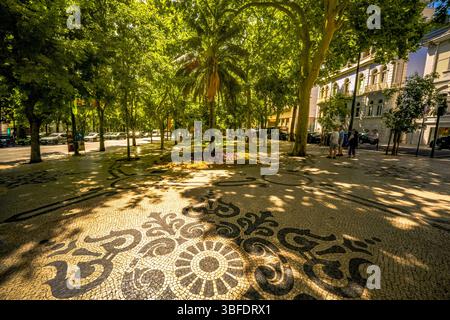 Verzierte portugiesische Mosaikpflastermuster unter Baumschatten auf dem berühmten Boulevard Avenida da Liberdade im Zentrum von Lissabon, Portugal Stockfoto