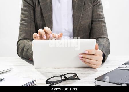 Nahaufnahme einer Frau, die einen Tablet-Computer hält. Geschäftsfrau, die am Schreibtisch arbeitet. Geschäftsfrau im Anzug an ihrem Arbeitsplatz im Büro. Manager mit Digital Stockfoto