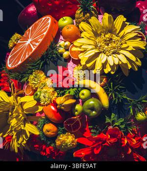 Farbenfrohe Anordnung von tropischen Früchten und künstlichen Blumen bei hellem Tageslicht Stockfoto