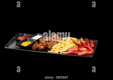 Bratwürste Pommes frites und Grillflügel mit Saucen auf einem großen Teller Stockfoto