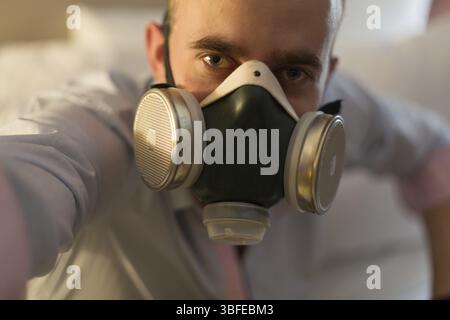 Hübscher junger, stilvoller kaukasischer Mann in Atemschutzmaske auf dem Bett im Schlafzimmer Stockfoto
