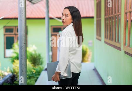 Eine selbstbewusste Frau dreht sich um und blickt zurück, während sie einen Laptop hält. Das Foto vermittelt Fokus, Bewusstsein und Professionalität. Stockfoto