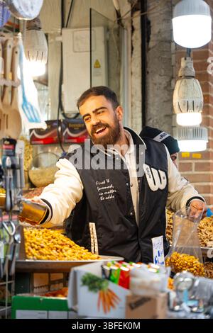 Teheran, Iran - 12. November 2023: Bärtiger Verkäufer, der am Marktstand fröhlich gemischte Nüsse schöpft Stockfoto