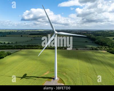 Weiße Windkraftanlage erzeugt erneuerbare Energie auf bebauten Feldern und wirft unter blauem Himmel mit Wolken einen Schatten auf die Pflanzen darunter Stockfoto