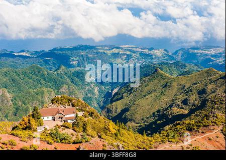 Üppige grüne Hügel und Täler erstrecken sich über den Horizont in Madeira, mit einem malerischen Haus auf einem Hügel. Die Szene zeigt die Natur der Insel Stockfoto