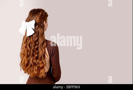 Frau mit langen welligen roten Haaren, die große weiße Schleife trägt, Rückansicht, neutraler Hintergrund, Konzept der Haarmode, Schönheitssalon, Friseur Stockfoto