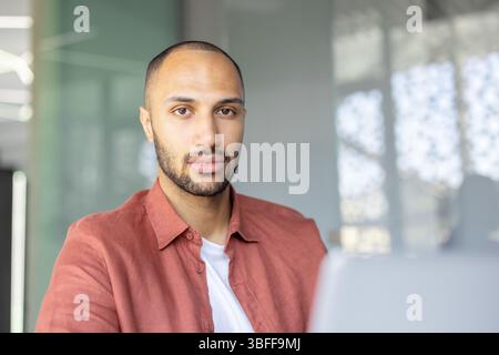 Ein ernsthaft aussehender Mann mit kurzem Bart, der ein rotes Hemd trägt, schaut aufmerksam in die Kamera. Stockfoto