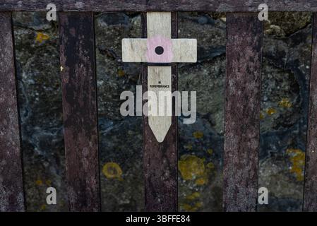 Kleines hölzernes Gedenkkreuz mit der Aufschrift „in Remembrance“ und einem Mohn, das auf einer öffentlichen Bank zu Ehren gefallener Soldaten am Gedenktag platziert wird. Stockfoto