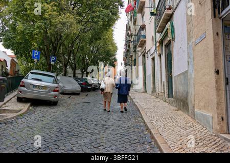 Zwei ältere Menschen laufen eine enge, gepflasterte Straße im Stadtteil Alfama in Lissabon, Portugal. Die Straße ist gekennzeichnet durch Stepped, mu Stockfoto