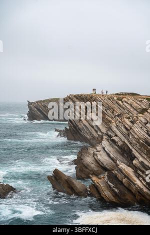 Peniche, Portugal - 12. Mai 2024: Einige Touristen stehen am Rande der riesigen, mehrschichtigen Klippen in Peniche, Portugal, mit Blick auf das turbulente Meer b Stockfoto