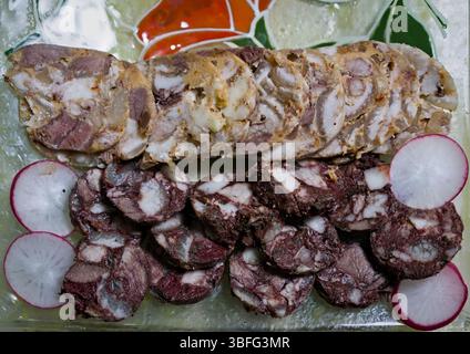 Schweinekuterie: In Scheiben geschnittener Käse und Blutwurst auf Glasschale mit Radieschengarnitur Stockfoto