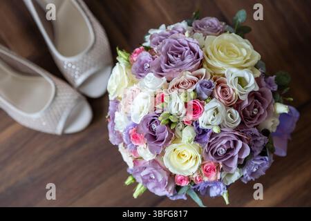 Brautstrauß aus pastellfarbenen Rosen mit Hochzeitsschuhen. Ein Blick von oben auf einen eleganten pastellfarbenen Brautstrauß mit Rosen in Lavendeltönen, weiß Stockfoto