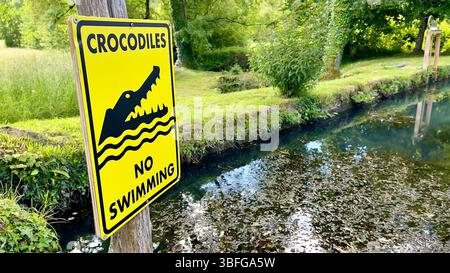 Ein etwas ironisches Schild in der Dordogne, Frankreich, das vor den Gefahren von Krokodilen warnt, neben einem beliebten Wanderweg, auf dem sich Besucher gerne abkühlen Stockfoto