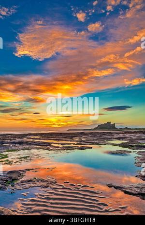 Ein Blick bei Sonnenaufgang auf Bamburgh Beach in Northumberland bei Ebbe in Richtung Bamburgh Castle mit einem wunderschönen Sonnenaufgangshimmel Stockfoto