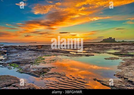 Ein Blick bei Sonnenaufgang auf Bamburgh Beach in Northumberland bei Ebbe in Richtung Bamburgh Castle mit einem wunderschönen Sonnenaufgangshimmel Stockfoto