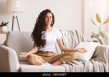 Friedliche Brünette Dame auf der Couch sitzend, meditierend Stockfoto