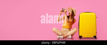 Glückliche Frau, die Fotos mit der Kamera macht und neben dem Gepäck sitzt Stockfoto