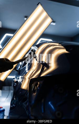 Der Techniker verwendet PDR-Werkzeuge, um Dellen von der Motorhaube während der lacklosen Reparatur der Dellen zu entfernen. Bei der lacklosen Dellen-Reparatur bei PDR werden Dellen unter hellen Stellen angestoßen Stockfoto