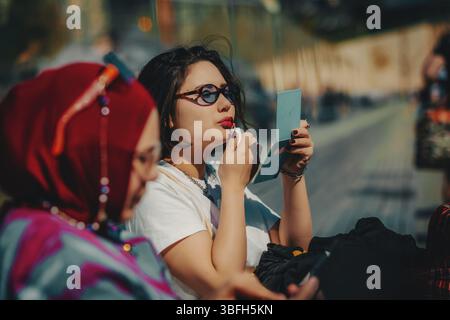 Eine junge Frau, die auf einer Bank sitzt und ihre Lippen malt Stockfoto