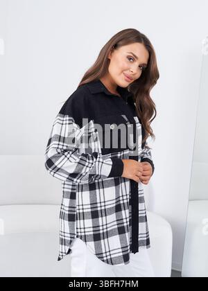 Charmante Brünette posiert in einem stilvollen karierten Hemd vor minimalistischem Hintergrund Stockfoto